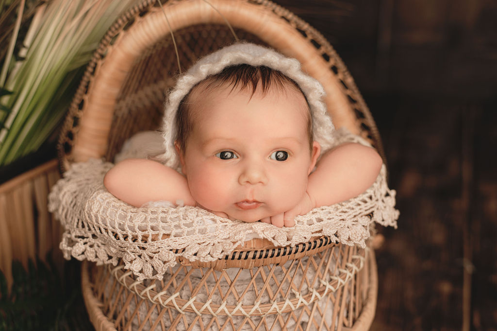 newborn baby in neutral bonnet laying on her arms in a basket Pediatric Dentist Burlington