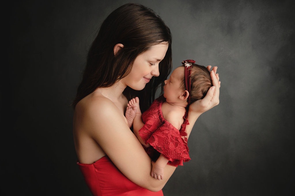 mom in red gown holding her baby girl in a matching outfit and looking at her Midwives of Oakville