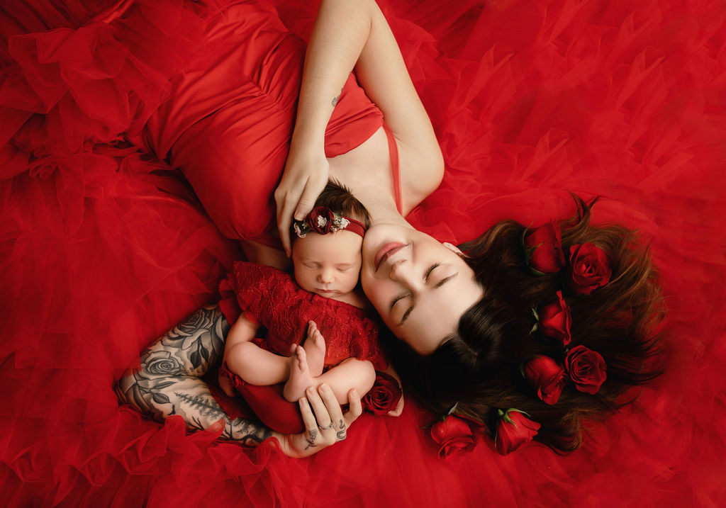 mom laying on the ground in a red gown with her newborn snuggling her Midwives of Oakville